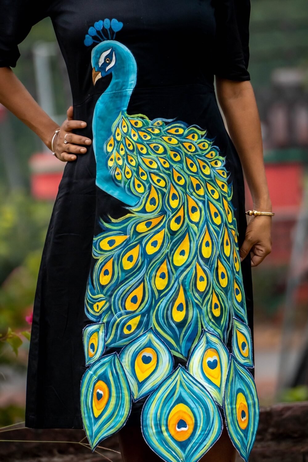 Close-up shot showing intricate hand painted 3D peacock feather details on a black cotton dress