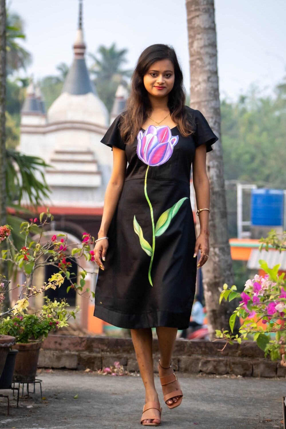 Front view of a woman walking in a handpainted 3D tulip black Malai Cotton dress