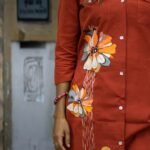 lose-up of three large artisan hand-painted floral motifs in ochre, cream, grey, and orange with vertical white line detailing on a rust orange button-down blazer tunic