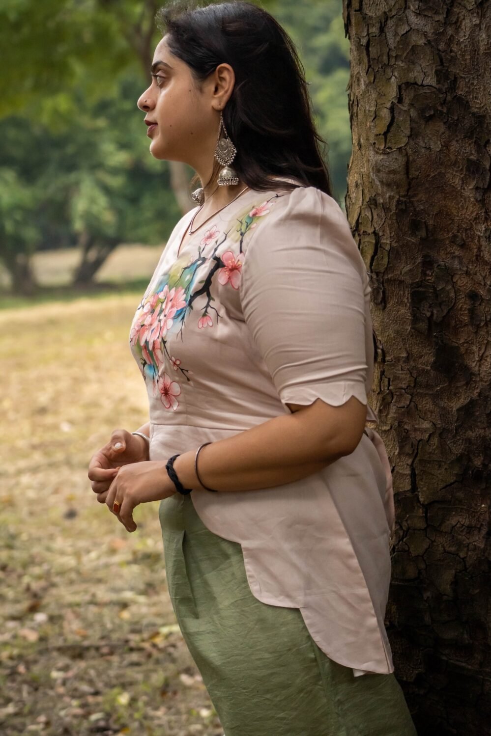 Side profile view highlighting the asymmetrical scalloped hemline and puff sleeve details of a beige hand-painted top.