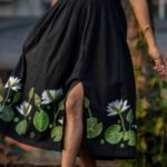 Close-up shot showing the front side slit and hand-painted water lily motifs on a black cotton midi dress