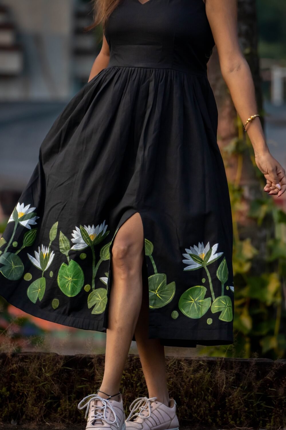 Close-up shot showing the front side slit and hand-painted water lily motifs on a black cotton midi dress
