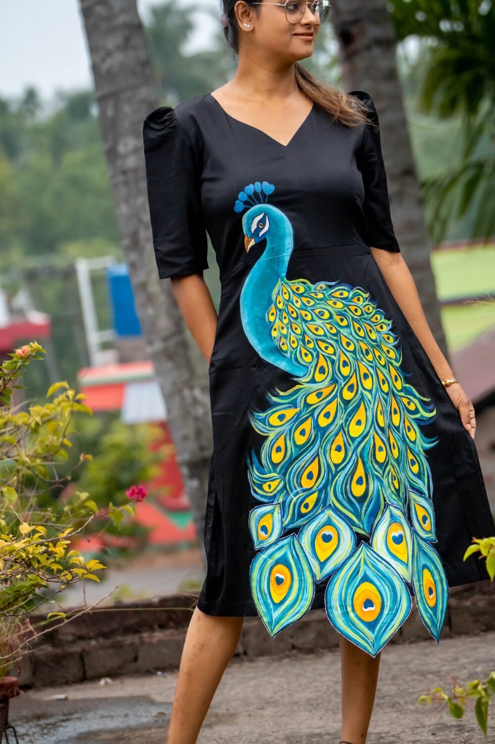 Three-quarter shot of a woman posing outdoors in a black hand-painted peacock Malai Cotton dress