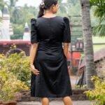 Back view of a black knee-length Malai Cotton midi dress showing puff sleeves and back zip detail