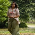 Full standing shot of a woman walking in a park wearing an artisanal hand-painted blossom beige scallop top co-ord set with wide-leg pants.