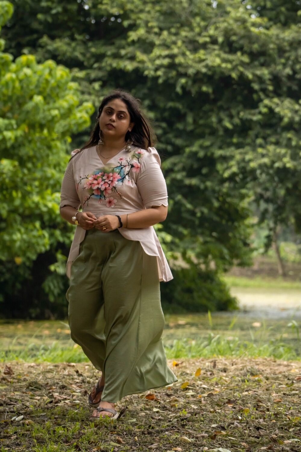 Full standing shot of a woman walking in a park wearing an artisanal hand-painted blossom beige scallop top co-ord set with wide-leg pants.