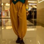Close-up of gathered yellow harem pants with an elasticated ankle cuff, paired with brown casual shoes on a reflective indoor floor