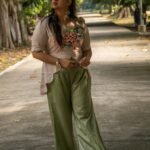 Candid full-length shot of a woman looking away, wearing a hand-painted beige blossom scallop top and sage green trousers.