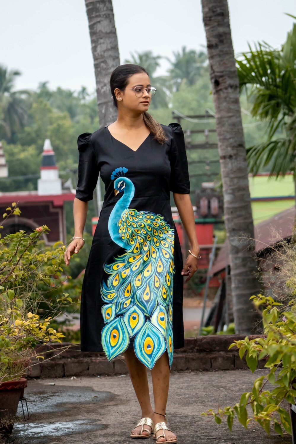 Full-length shot of a woman walking outdoors in a hand painted 3D peacock black midi dress
