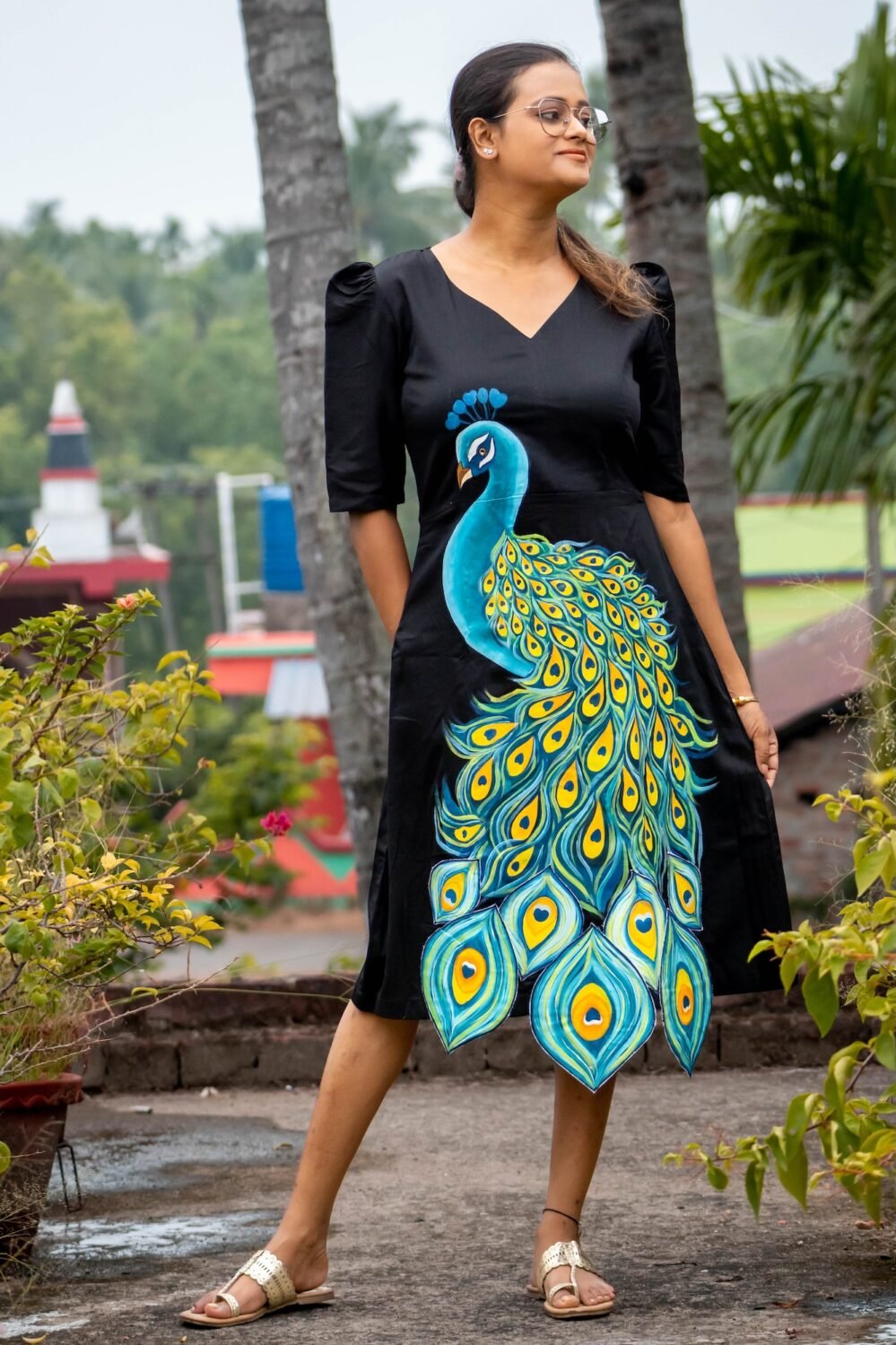 Front view of a model posing in a black hand painted 3D peacock Malai Cotton dress with puff sleeves
