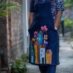 Close-up of hand-painted colorful cityscape and floral artwork on the front hem of the midnight blue cotton tunic