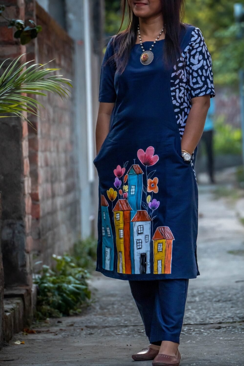 Close-up of hand-painted colorful cityscape and floral artwork on the front hem of the midnight blue cotton tunic