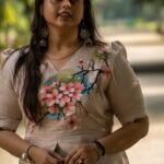 Medium shot of a woman wearing a beige hand-painted floral scallop top with scalloped sleeves paired with silver traditional earrings.