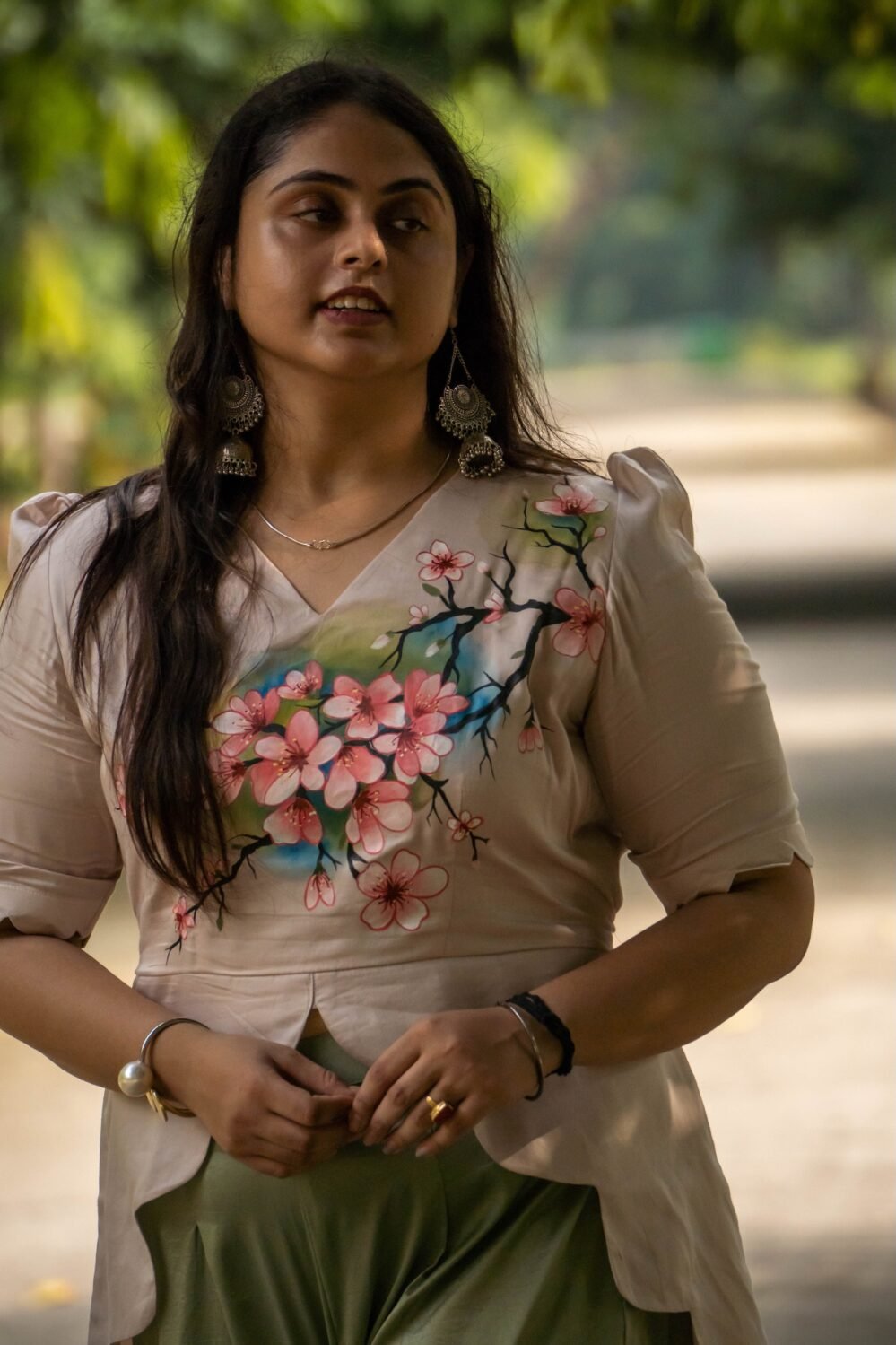 Medium shot of a woman wearing a beige hand-painted floral scallop top with scalloped sleeves paired with silver traditional earrings.