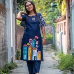 Woman posing in a navy blue cotton tunic with hand-painted house motifs and a batik sleeve detail.