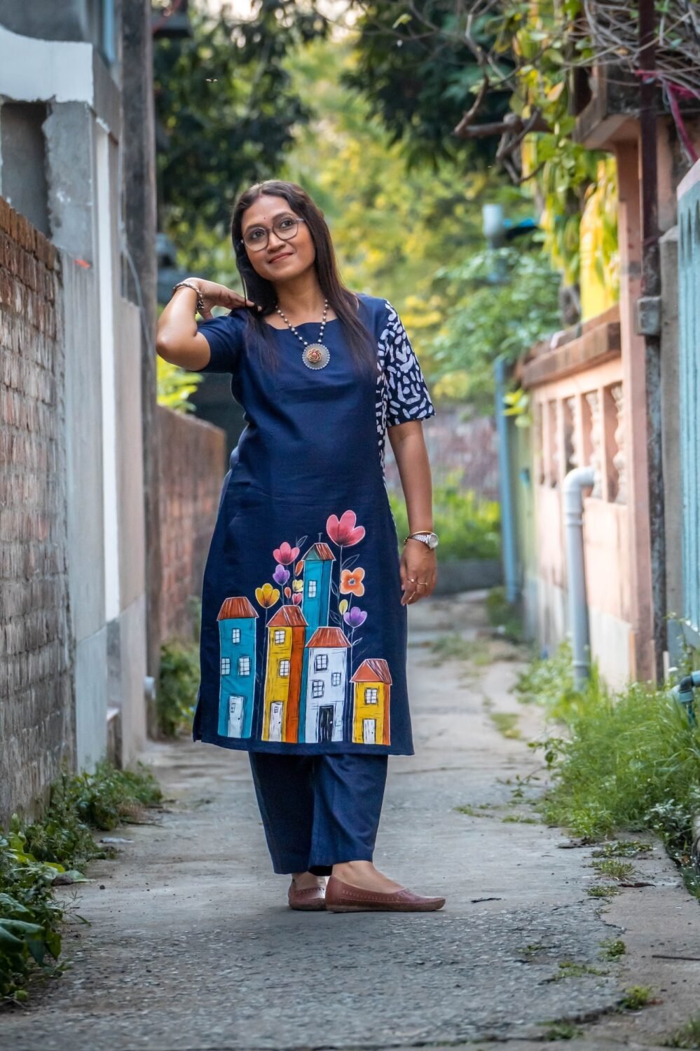 Woman posing in a navy blue cotton tunic with hand-painted house motifs and a batik sleeve detail.