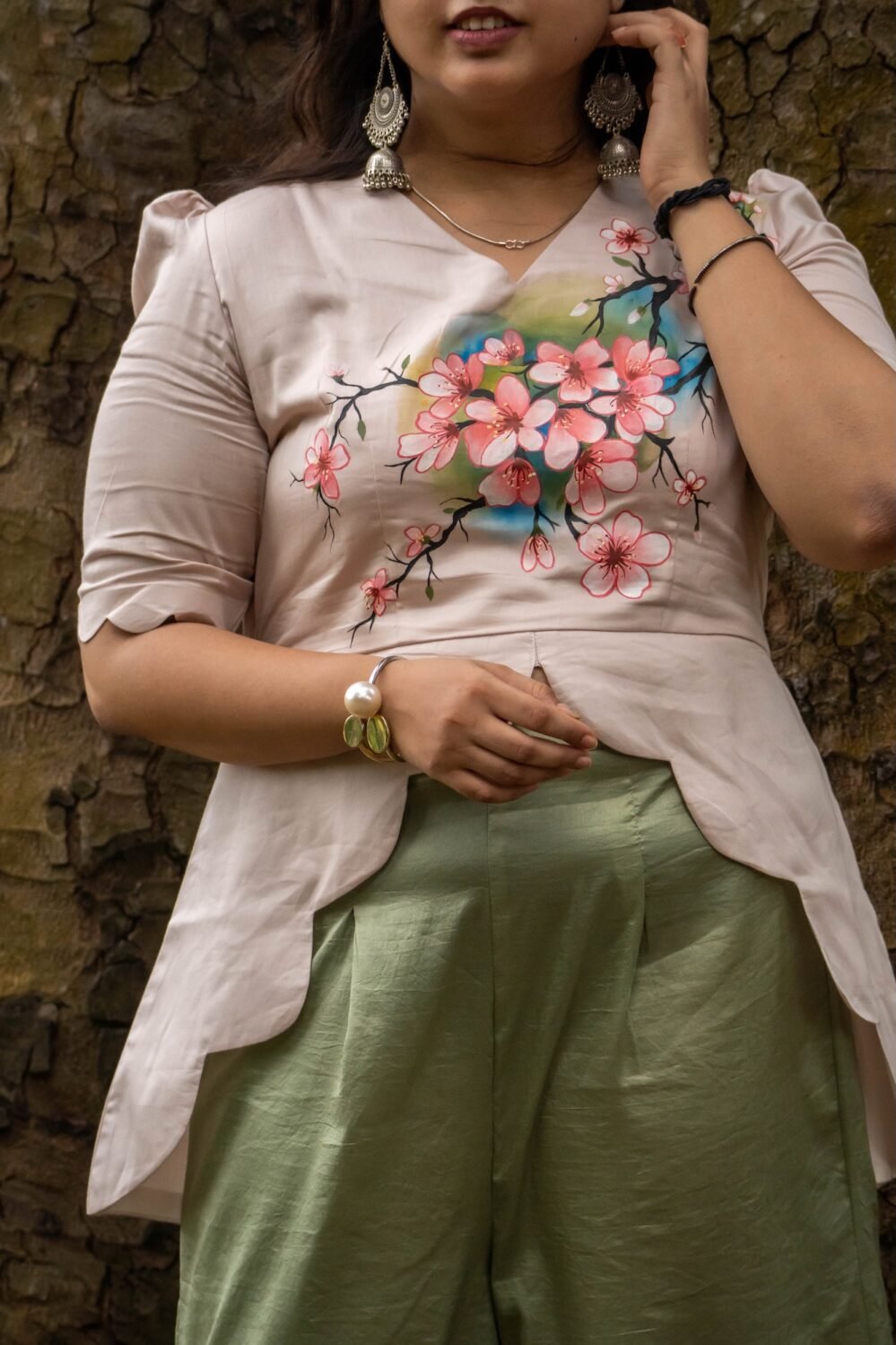Close-up of the front bodice showing detailed hand-painted pink cherry blossom flowers on a beige scallop top with pearl bracelet accessory