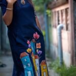 Detailed view of hand-painted turquoise, yellow, and orange houses with floral motifs on blue cotton fabric.
