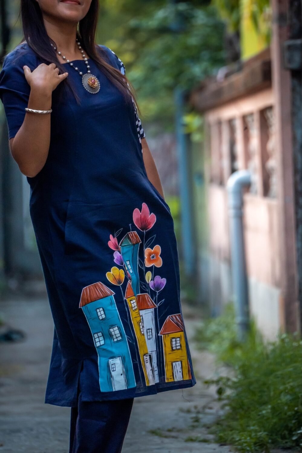 Detailed view of hand-painted turquoise, yellow, and orange houses with floral motifs on blue cotton fabric.
