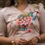 Close-up view of intricate hand-painted cherry blossom branch design across a V-neck beige scallop top.