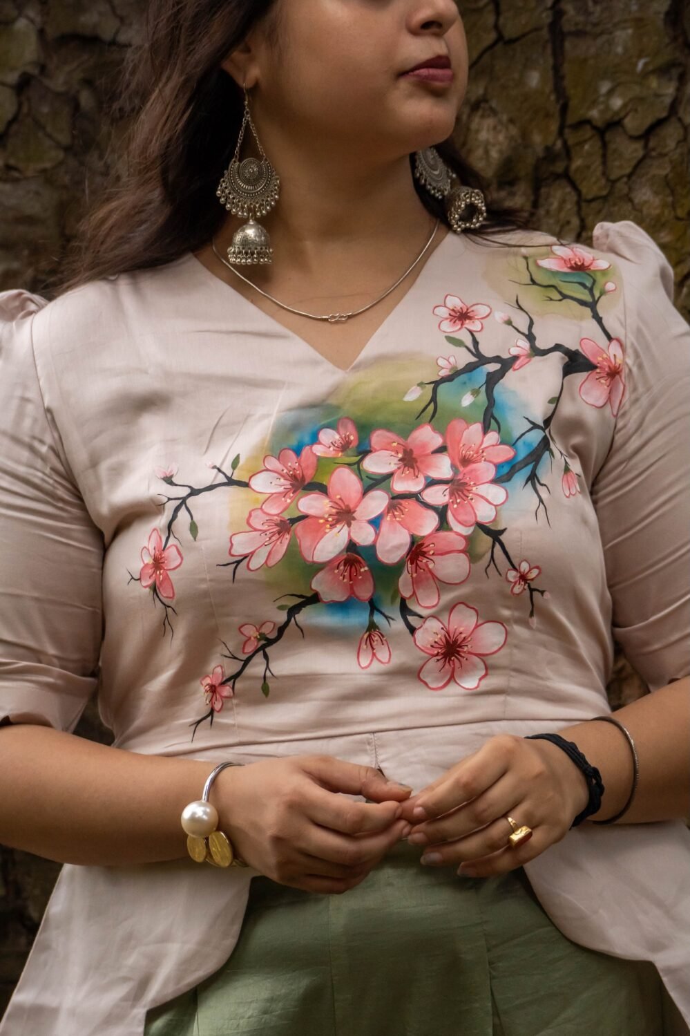 Close-up view of intricate hand-painted cherry blossom branch design across a V-neck beige scallop top.