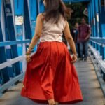 Back view of model twirling on a bridge showing the flowy fit of the red Malai Cotton skirt