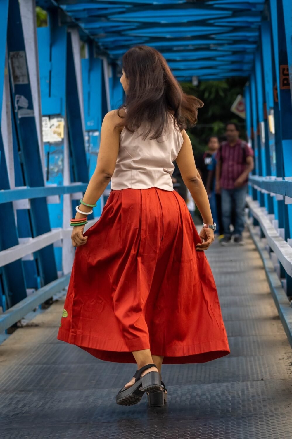 Back view of model twirling on a bridge showing the flowy fit of the red Malai Cotton skirt