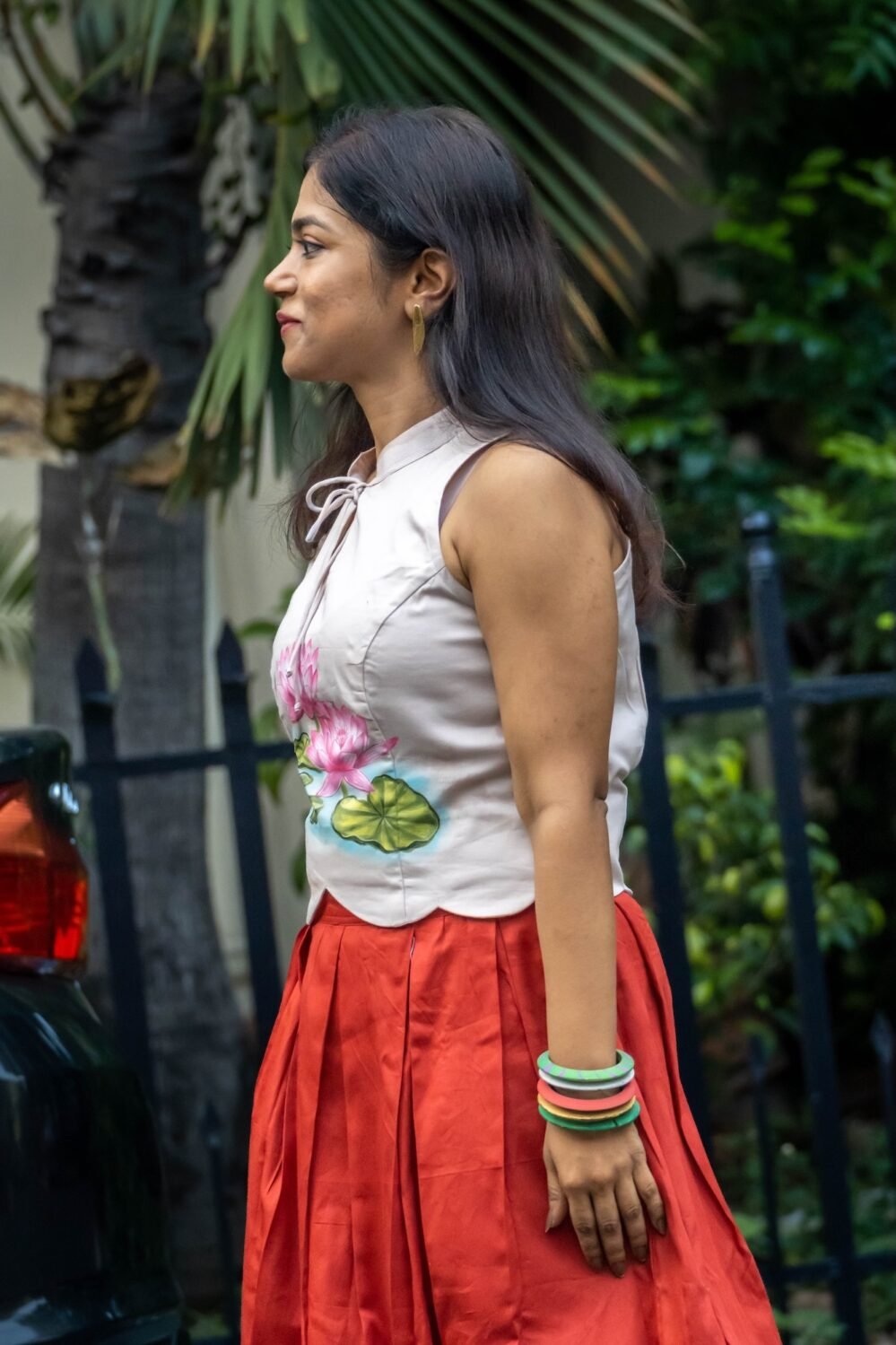 Side profile view of model wearing a sleeveless hand-painted lotus top with keyhole tie-up neckline and red skirt