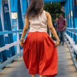 Model wearing hand-painted lotus skirt co-ord set walking across a blue metal bridge