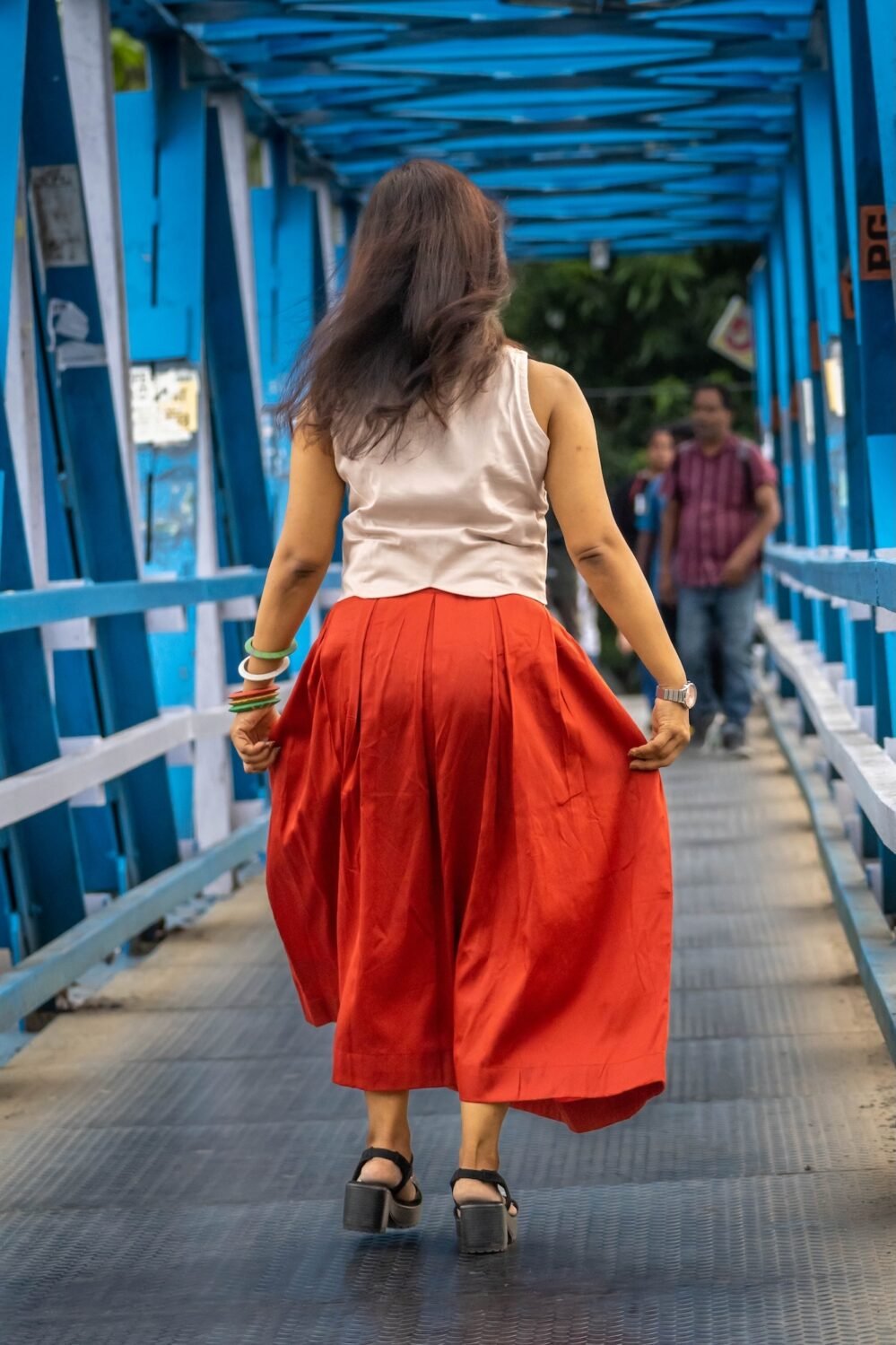 Model wearing hand-painted lotus skirt co-ord set walking across a blue metal bridge