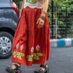 Lower body and skirt detail showing the hand-painted lotus border on a red flared skirt as the model walks outdoors