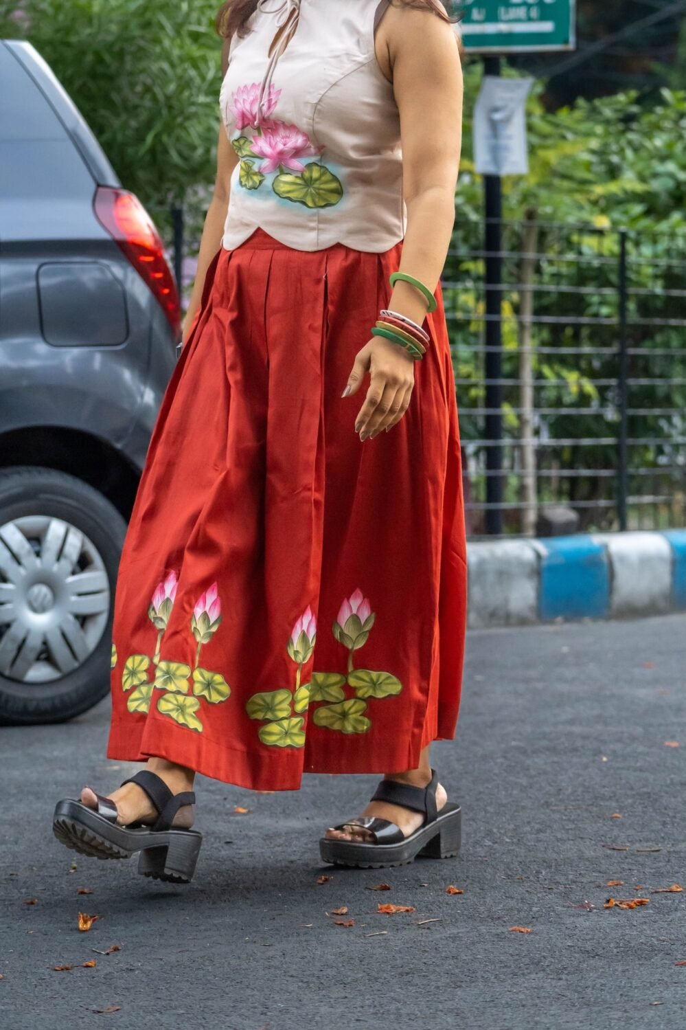 Lower body and skirt detail showing the hand-painted lotus border on a red flared skirt as the model walks outdoors