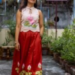 Model walking outdoors wearing hand-painted lotus halter top with flared red skirt
