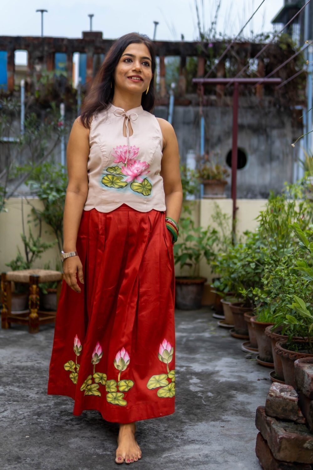 Model walking outdoors wearing hand-painted lotus halter top with flared red skirt