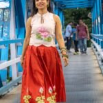 Model wearing hand-painted lotus skirt co-ord set walking across a blue metal bridge