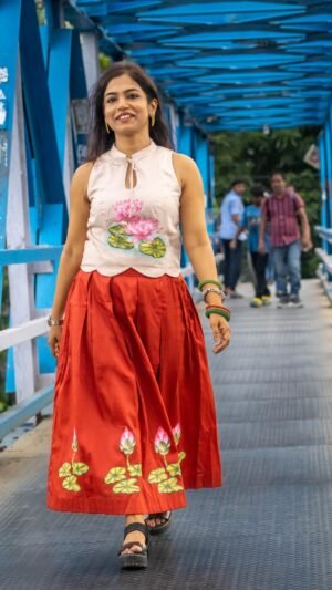Model wearing hand-painted lotus skirt co-ord set walking across a blue metal bridge