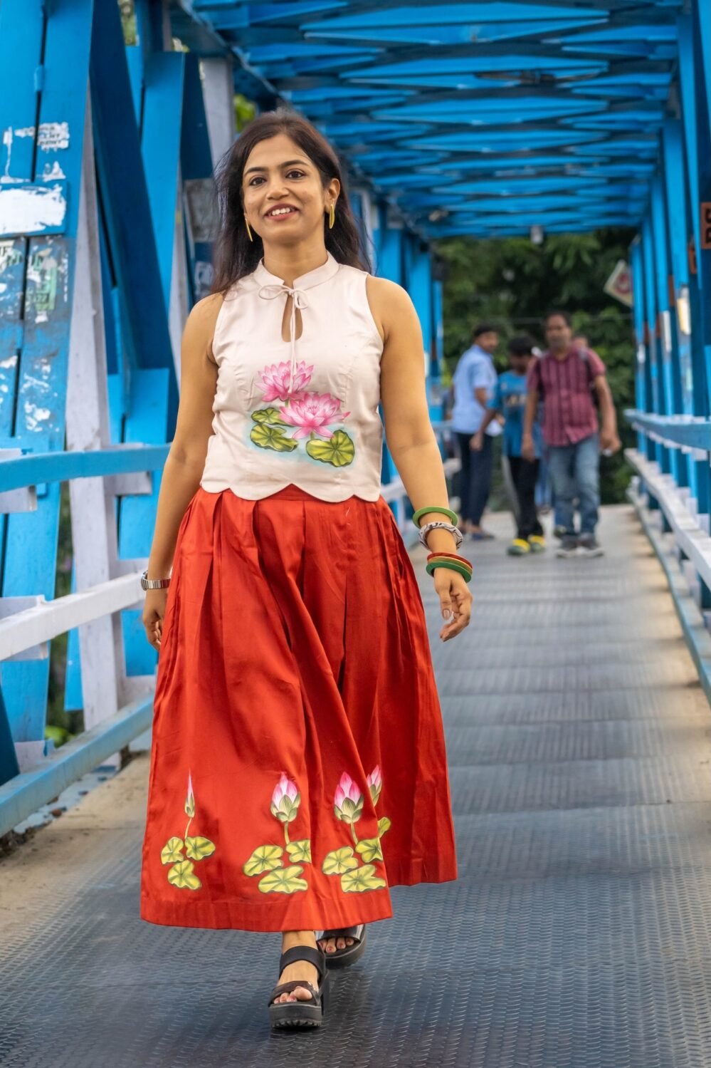 Model wearing hand-painted lotus skirt co-ord set walking across a blue metal bridge