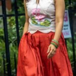 Mid-length shot showing the keyhole halter neck and hand-painted lotus motif on the top paired with a red pleated skirt