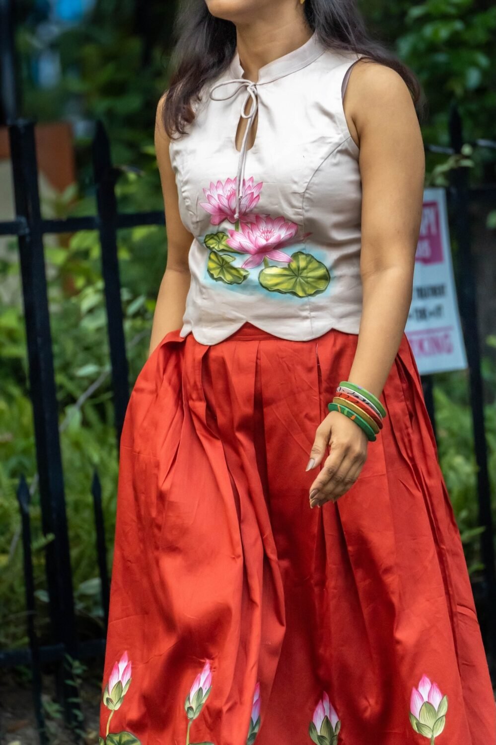 Mid-length shot showing the keyhole halter neck and hand-painted lotus motif on the top paired with a red pleated skirt