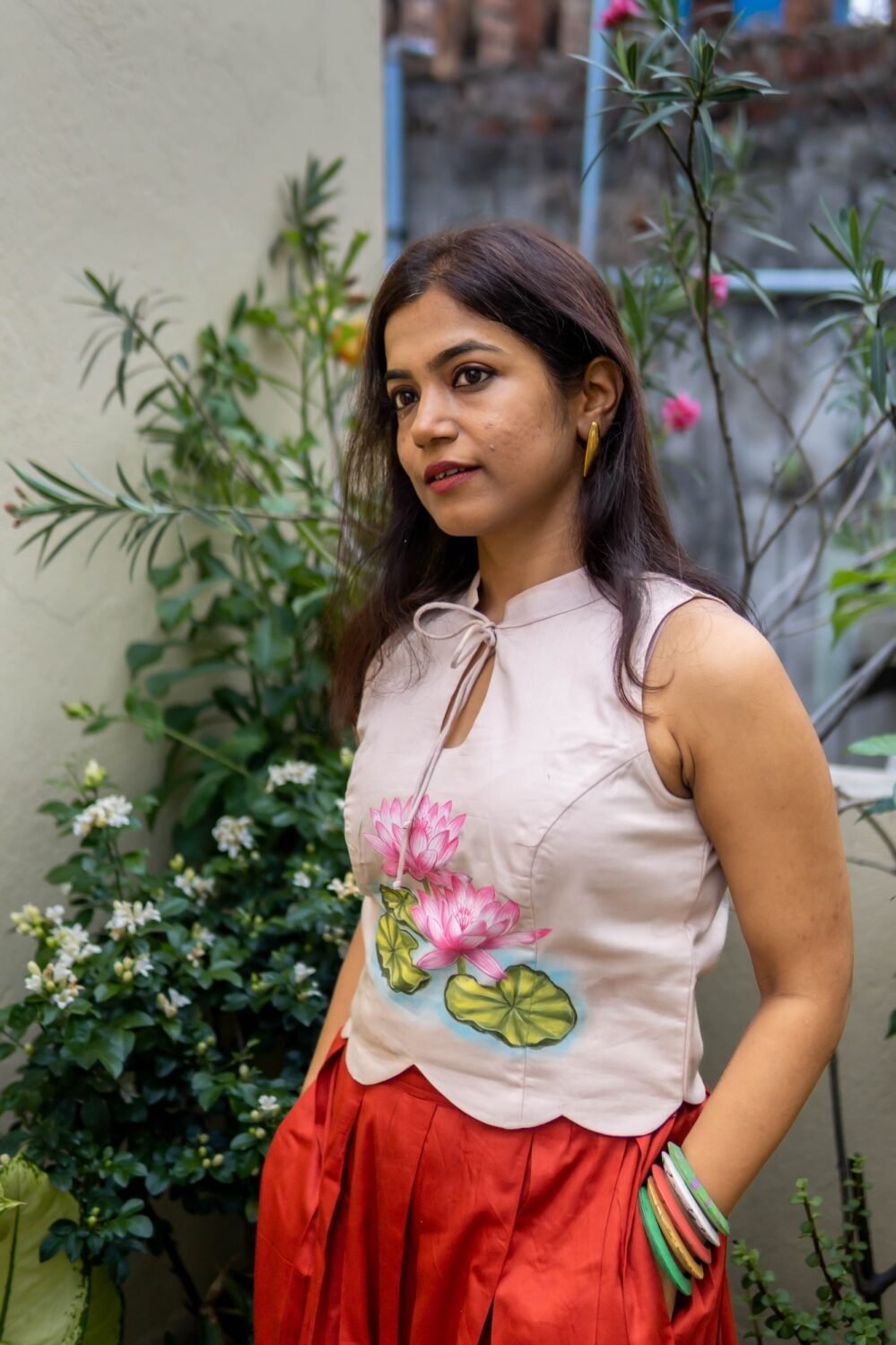 Side profile of model in off-white hand-painted lotus halter top and red skirt