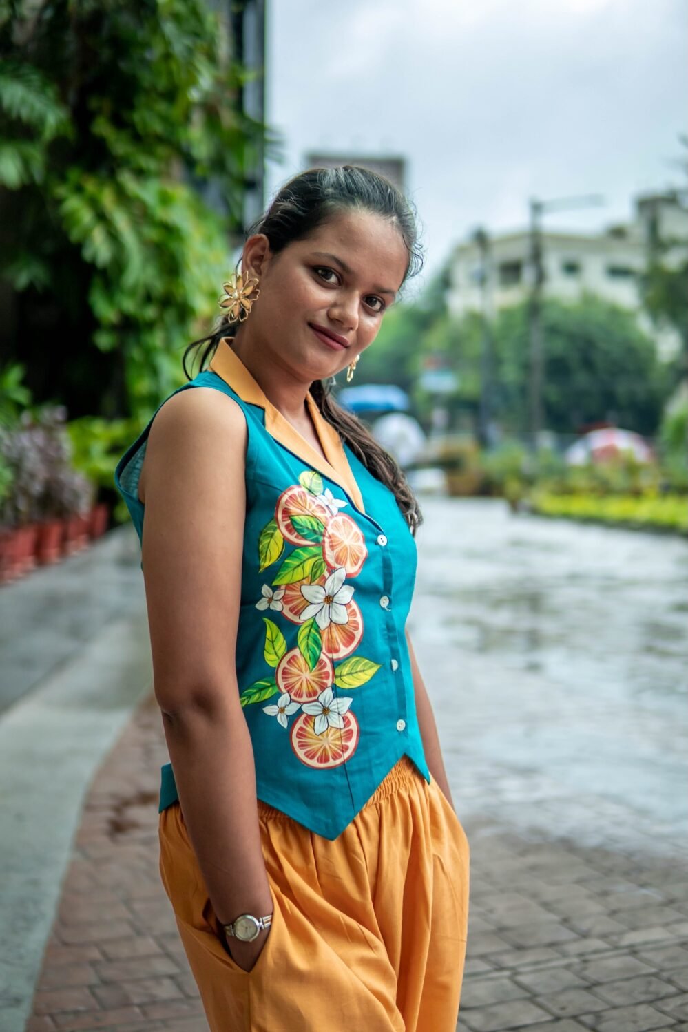 Side profile of a woman posing outdoors in a teal hand-painted waistcoat with a yellow collar and matching yellow pants