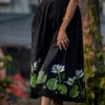Detailed close-up of hand-painted white water lilies and green leaves along the hem of a black dress