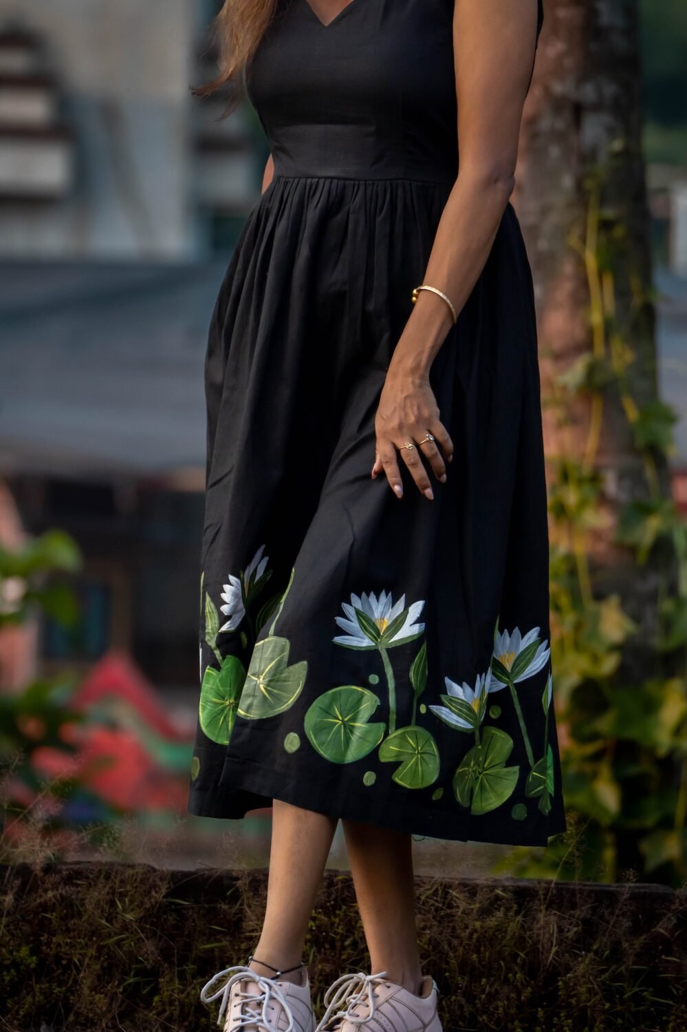 Detailed close-up of hand-painted white water lilies and green leaves along the hem of a black dress