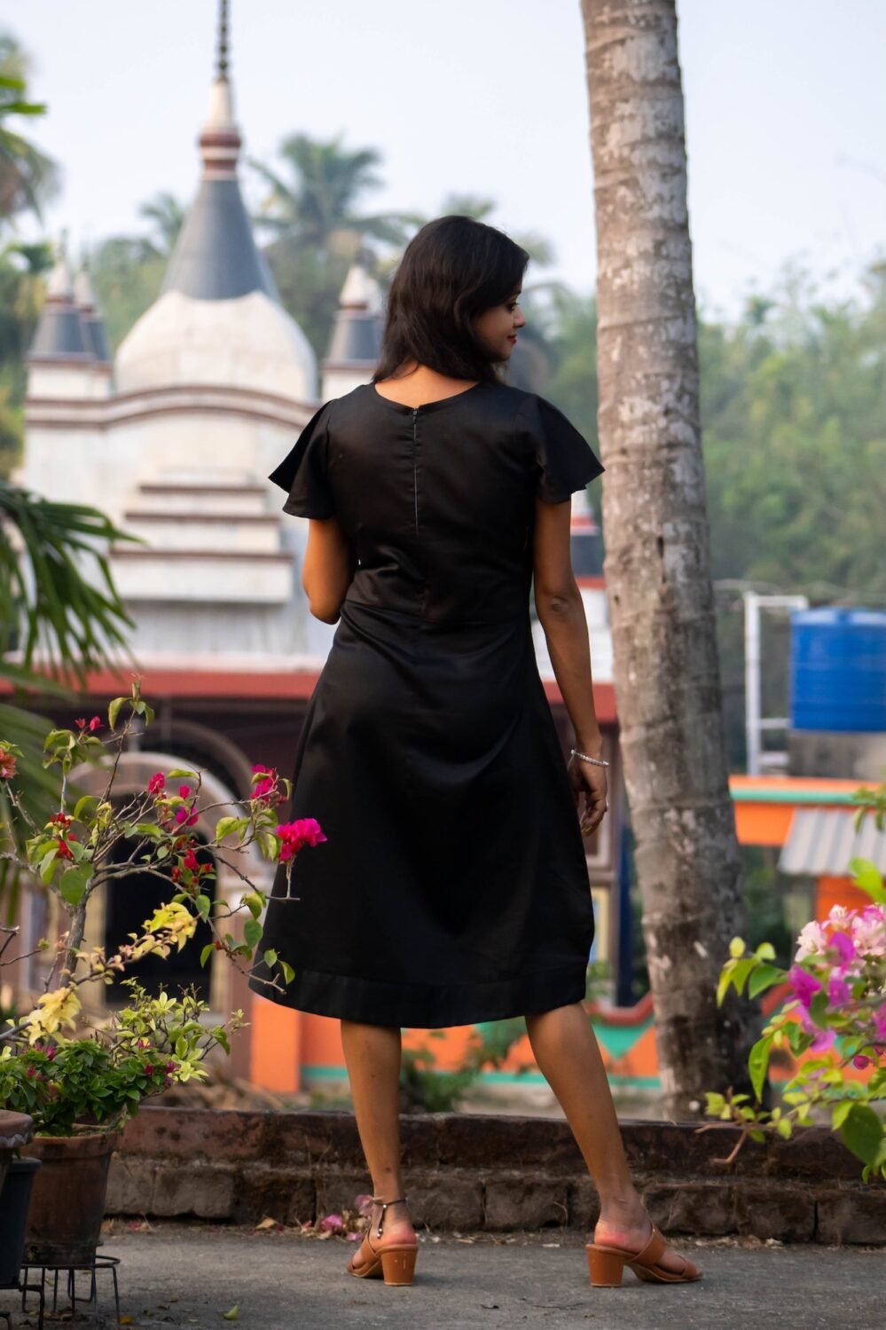 Back view of model wearing a black Malai Cotton dress outdoors