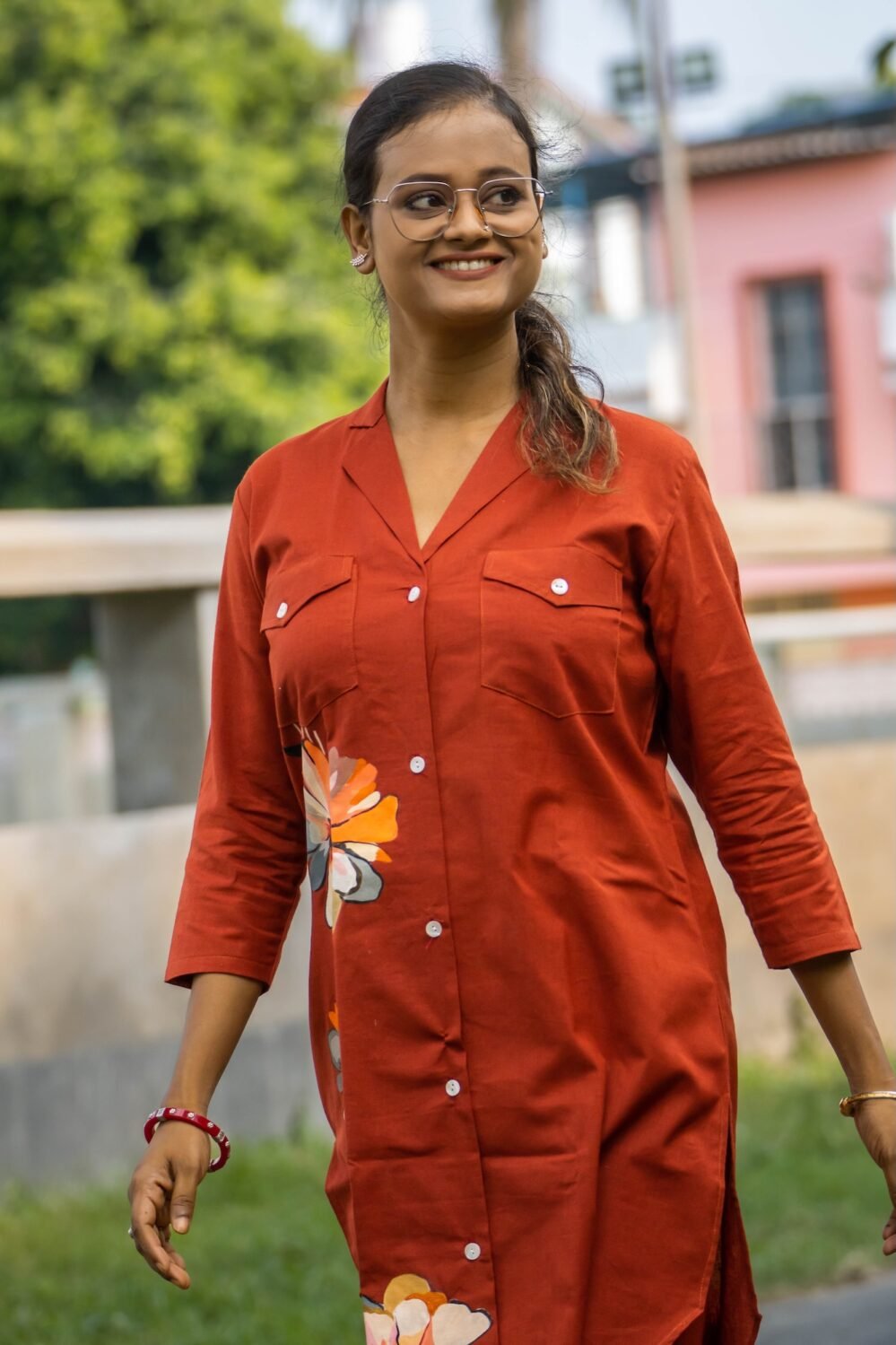Mid-shot of a smiling woman wearing a terracotta button-down blazer tunic with structured lapel collar, two chest pockets, and hand-painted floral detailing on the front