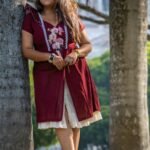 Full view of Mridu hand-painted orchid maroon cotton dress leaning on a tree.