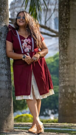 Full view of Mridu hand-painted orchid maroon cotton dress leaning on a tree.