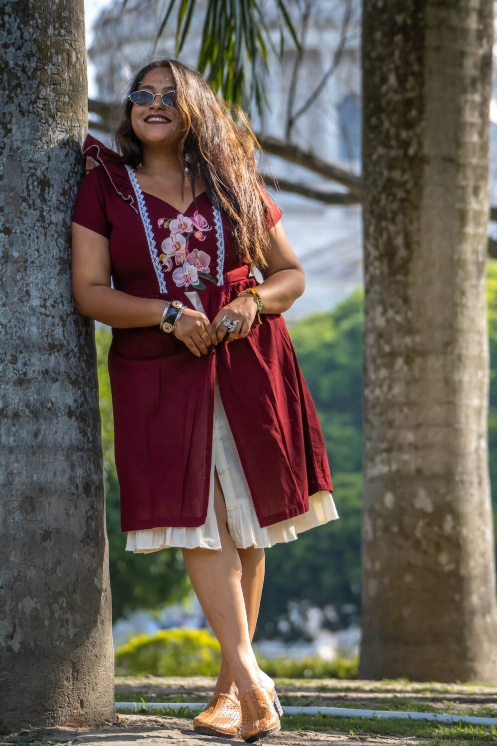 Full view of Mridu hand-painted orchid maroon cotton dress leaning on a tree.