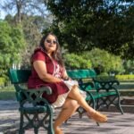 Model seated on a bench wearing Mridu hand-painted maroon cotton summer dress.