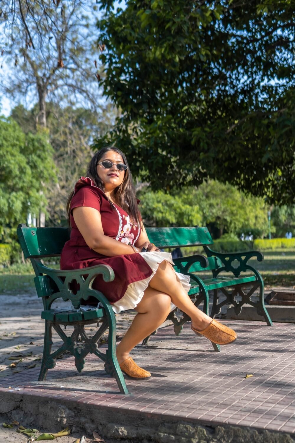 Model seated on a bench wearing Mridu hand-painted maroon cotton summer dress.